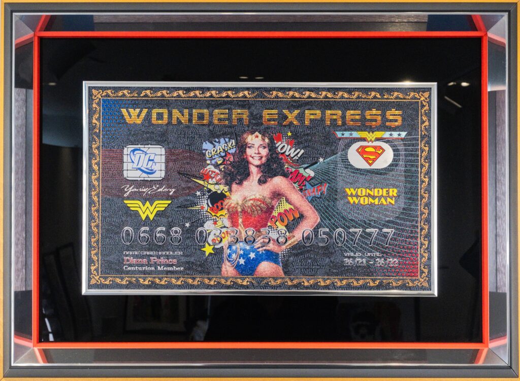Yaniv Edery – Wonder Express Dit opvallende kunstwerk van Yaniv Edery brengt iconische popcultuur en luxe samen in één gedurfde compositie. Centraal staat Wonder Woman, afgebeeld met haar herkenbare uitstraling en kracht. Omringd door stripsymbolen en geplaatst op een biljet dat lijkt op een creditcard, ontstaat een unieke mix van superheldenenergie en consumptie-ironisering. De kleurrijke details en de glanzende afwerking geven het werk een dynamische uitstraling. Woorden als Pow! en Wow!voegen een speels stripgevoel toe, terwijl de compositie tegelijk elegant en krachtig blijft. Het contrast tussen de serieuze achtergrond en de vrolijke pop-art details maakt dit werk spannend en veelzijdig. Edery weet hier niet alleen een heldin te tonen, maar ook een boodschap. Wonder Woman wordt een symbool voor kracht, vrouwelijkheid en onafhankelijkheid. Tegelijkertijd zet de combinatie met een luxueuze creditcard aan tot nadenken over consumptie, status en moderne waarden. Het is kunst met lagen: speels, krachtig en betekenisvol. Het werk bruist van energie en trekt direct de aandacht. Elke penseelstreek en elk detail dragen bij aan een verhaal dat balanceert tussen fantasie en realiteit. Wonder Express is geen gewone decoratie, maar een krachtig statement dat emoties oproept en nieuwsgierigheid wekt.