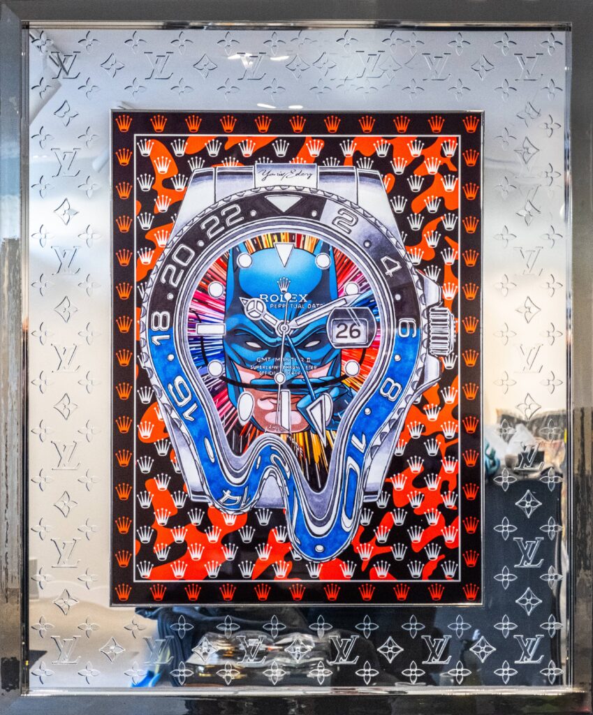 Rolex Batman Laser Cut – Yaniv Edery Rolex Batman Laser Cut is een explosie van luxe, kracht en symboliek. Het kunstwerk toont een vervormde Rolex GMT-Master, gecombineerd met iconische patronen van Louis Vuitton. Deze samensmelting van horlogerie en high fashion creëert een adembenemend visueel spektakel. Bovendien maakt de precisie van de laser cut het werk indrukwekkend modern. De felblauwe tinten contrasteren scherp met het vurige rood en zwart, waardoor de energie van het doek onmiddellijk voelbaar wordt. De Rolex in het midden lijkt te smelten, als een verwijzing naar tijd die vervormt. Dit versterkt de boodschap: luxe is niet alleen bezit, maar ook beleving. Het spel van symmetrie en chaos maakt het werk intrigerend. Elke blik onthult nieuwe details, elke lijn benadrukt vakmanschap. Daarom is Rolex Batman Laser Cut meer dan een kunstwerk; het is een statement over tijd, macht en identiteit. De reflecterende lijst, voorzien van het Louis Vuitton-patroon, verhoogt het gevoel van exclusiviteit. Het werk straalt verfijning uit, maar daagt ook uit. Want enerzijds toont het luxe, anderzijds breekt het deze traditie open door vervorming. Daardoor ontstaat een krachtige dialoog tussen traditie en vernieuwing. Dit meesterwerk is ideaal voor verzamelaars die durven kiezen. Het combineert modern design, iconische merken en artistieke vrijheid. Met krachtige kleuren, scherpe lijnen en opvallende details trekt het altijd aandacht.