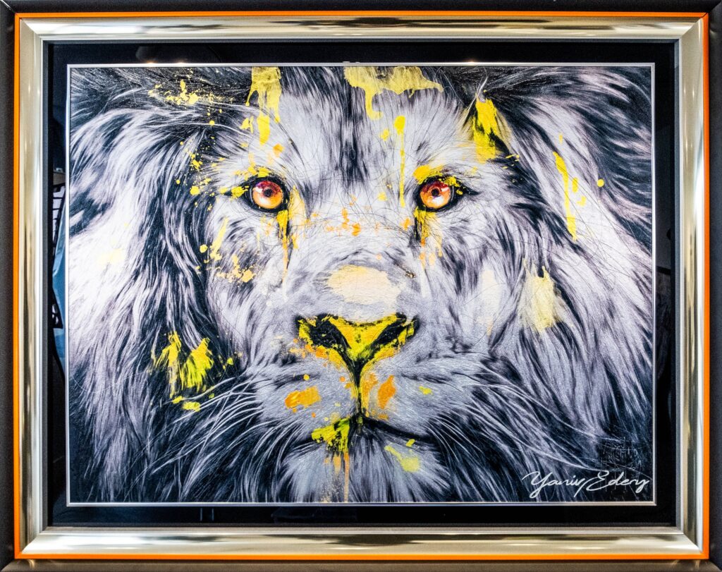 Yaniv Edery – Lion Yellow Face Het kunstwerk Lion Yellow Face van Yaniv Edery straalt pure kracht uit. Een indrukwekkend portret van een leeuw, vastgelegd in zwart-wit met opvallende gele accenten. De intensiteit van de ogen grijpt de toeschouwer direct vast. De expressieve penseelstreken en de dynamische verfspatten zorgen voor een rauw en energiek effect. Edery kiest bewust voor contrasterende kleuren. Het zachte grijs en wit staan tegenover felgeel, waardoor de leeuw een bijna mythische uitstraling krijgt. Dit gebruik van kleur versterkt de symboliek van moed, macht en wijsheid. Bovendien brengen de accenten beweging in het werk, alsof de leeuw elk moment tot leven kan komen. Het gezicht van de leeuw vult het hele doek en dwingt zo volledige aandacht. Elke blik onthult iets nieuws: kracht, vastberadenheid, maar ook een zekere rust. Door deze gelaagdheid blijft het kunstwerk fascineren. Het gebruik van reliëf geeft extra diepte en laat details nog sterker naar voren komen. Lion Yellow Face is meer dan een portret. Het is een moderne interpretatie van de koning der dieren, weergegeven als symbool van dominantie en schoonheid. De combinatie van realisme en abstractie geeft het werk een unieke en hedendaagse uitstraling. Dit maakt het kunstwerk niet alleen visueel sterk, maar ook inhoudelijk betekenisvol. Met dit werk nodigt Yaniv Edery de kijker uit om kracht en energie opnieuw te beleven. Het kunstwerk is expressief, krachtig en tegelijk elegant.