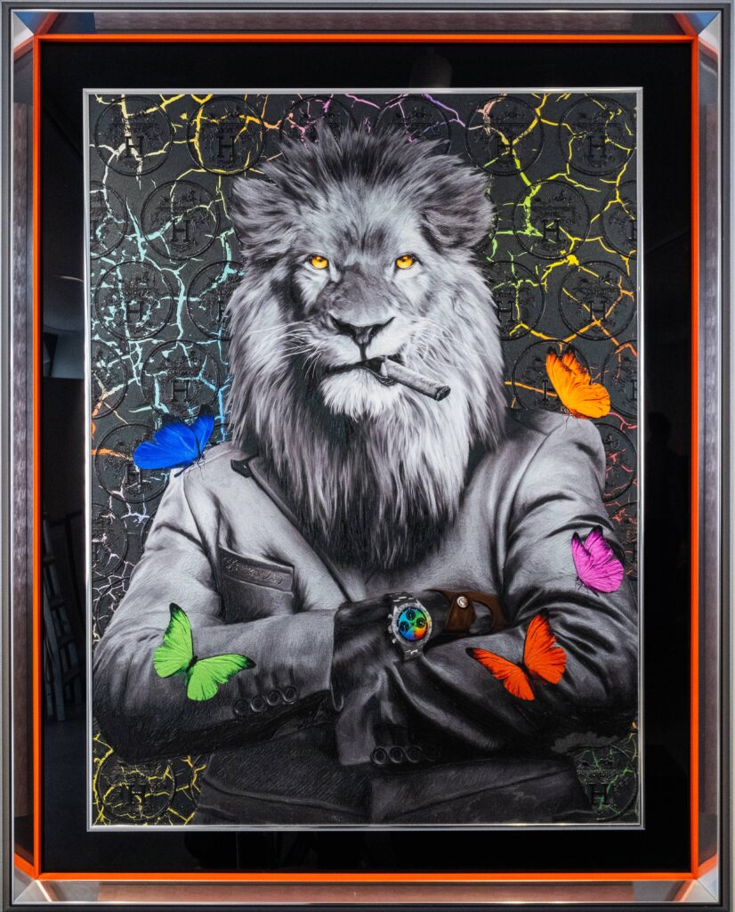 Yaniv Edery – Lion Multicolor Butterfly Dit indrukwekkende kunstwerk van Yaniv Edery toont een trotse leeuw die kracht en zelfvertrouwen uitstraalt. De leeuw, gehuld in een strak zwart pak en met een sigaar tussen zijn tanden, kijkt de toeschouwer met een intense blik aan. Zijn gouden ogen vangen direct de aandacht en benadrukken zijn majesteitelijke aanwezigheid. Wat dit werk bijzonder maakt, zijn de kleurrijke vlinders die rond de leeuw dansen. Felblauwe, groene, oranje, roze en paarse accenten contrasteren met het monochrome zwart-wit van de leeuw zelf. Deze speelse toevoeging verzacht het krachtige beeld en brengt balans tussen dominantie en lichtheid. Het resultaat is een harmonieus en verrassend geheel. Edery speelt met tegenstellingen: macht tegenover kwetsbaarheid, ernst tegenover speelsheid. De vlinders, vaak symbool voor transformatie en vrijheid, voegen een poëtische laag toe aan het werk. Ze brengen lucht en beweging in de compositie, terwijl de leeuw onverstoorbaar en vastberaden blijft. Dit contrast geeft het kunstwerk diepte en maakt het gelaagd. De achtergrond, met zijn gebarsten textuur en subtiele glans, versterkt de dramatische sfeer. Elk detail, van de haren in de manen tot de glans van het horloge om zijn pols, is zorgvuldig uitgewerkt. Lion Multicolor Butterfly is niet enkel een visueel spektakel, maar ook een krachtig symbool voor balans, luxe en persoonlijke kracht. Dit kunstwerk weet zowel te imponeren als te inspireren. Het vangt de essentie van kracht en verfijning, maar voegt er tegelijkertijd een speelse twist aan toe die steeds opnieuw verrast.