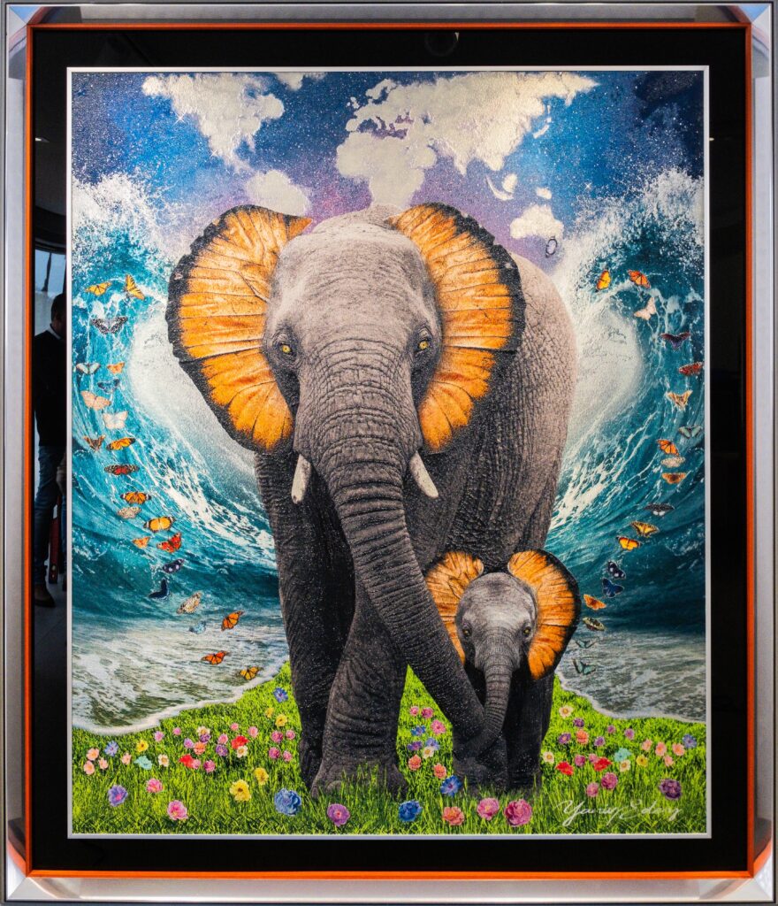 Yaniv Edery – Elephant Orange Black Ears Het werk Elephant Orange black ears  straalt kracht en tederheid uit. Twee olifanten staan centraal, hun oren opvallend omlijst door een intens oranje gloed. Dit detail geeft het werk een levendige en unieke uitstraling. De achtergrond toont een dynamische golf die symbool staat voor natuurkracht en beweging. Tegelijkertijd zorgen de kleurrijke bloemen en vlinders aan de voorgrond voor een zachte balans. Hierdoor ontstaat een krachtig contrast tussen energie en harmonie. De olifanten zijn meer dan enkel dieren in dit kunstwerk. Zij symboliseren wijsheid, bescherming en verbondenheid. De moeder en haar jong staan als metafoor voor familie en continuïteit. Het gebruik van sprankelende kleuren versterkt deze boodschap. Daardoor wordt het werk niet alleen visueel indrukwekkend, maar ook emotioneel betekenisvol. Dit kunstwerk toont duidelijk Edery’s signatuur. Zijn spel met kleur, textuur en symboliek geeft Elephant Orange een iconische uitstraling. De aandacht voor detail maakt dat elke blik nieuwe nuances onthult.