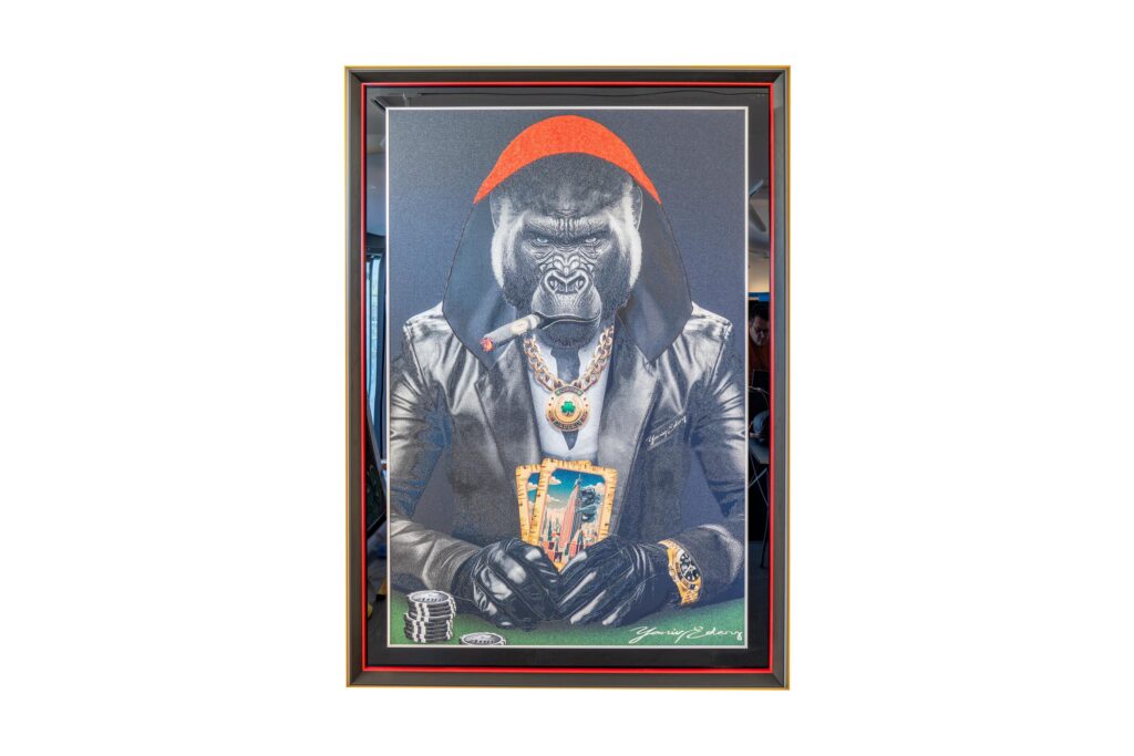 Yaniv Edery – Gorilla Poker Cape Red is een krachtig kunstwerk dat dominantie, luxe en stijl samenbrengt. De imposante gorilla zit aan de pokertafel, gehuld in een stoere leren jas en een felrode cape. De details trekken meteen de aandacht: een grote gouden ketting, opvallende ringen en een sigaar die kracht en autoriteit symboliseert. De rode cape is niet alleen een stijlvol detail, maar ook een symbool van macht en leiderschap. Het maakt de gorilla tot een ware heerser van het spel. Daarbij versterken de felle contrasten en diepe kleuren de intensiteit van het werk. De blik van de gorilla is vastberaden en onverzettelijk. Hij straalt uit dat hij controle heeft over de kaarten en daarmee over de hele situatie. Het poker-thema geeft het kunstwerk een extra laag. Poker draait om risico, strategie en durf. Precies deze elementen weet Edery te vertalen naar zijn kunst. De kaarten, de fiches en de houding van de gorilla brengen spanning en elegantie samen. Het werk voelt tegelijk speels én indrukwekkend, een combinatie die blijft fascineren. Elk detail in dit werk is zorgvuldig gekozen. Van de glans op de sieraden tot de scherpe contouren van de gorilla’s gezicht, alles ademt luxe en kracht. Dit maakt het kunstwerk niet alleen een visueel hoogtepunt, maar ook een verhaal over macht, lef en identiteit. Gorilla Poker Cape Red is een blikvanger die een ruimte volledig transformeert. Het straalt energie, zelfvertrouwen en karakter uit, en nodigt uit tot gesprek en bewondering.