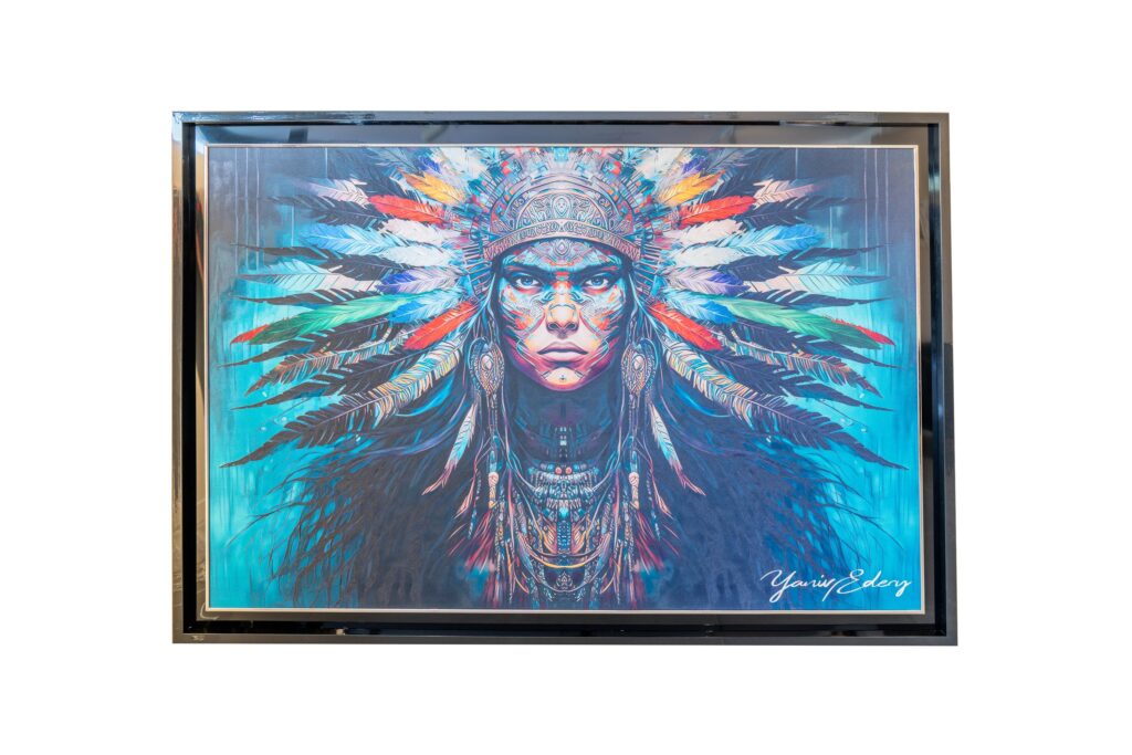 Yaniv Edery – Indian Blue Dit indrukwekkende kunstwerk van Yaniv Edery toont een krachtig portret van een inheemse krijger. Met een indringende blik, een rijk gedetailleerde tooi en een aura van mystiek, straalt het werk kracht, wijsheid en spiritualiteit uit. De combinatie van diepe blauwtinten en felle accenten geeft het geheel een moderne en expressieve uitstraling. De hoofdtooi, versierd met kleurrijke veren, symboliseert trots, traditie en identiteit. Elke veer lijkt zorgvuldig geplaatst en benadrukt de balans tussen natuur en cultuur. De intense blik van de krijger trekt direct de aandacht en laat de kijker niet onberoerd. Het portret is niet alleen visueel sterk, maar ook emotioneel geladen. De achtergrond in krachtige blauwtinten versterkt het gevoel van diepte en intensiteit. Het werk ademt een bijna spirituele energie uit, alsof de krijger uit de geschiedenis naar voren treedt om zijn verhaal te vertellen. Dit contrast tussen oude symboliek en moderne artistieke stijl maakt het kunstwerk uniek. Edery legt met dit werk de nadruk op respect, kracht en traditie, maar ook op transformatie en verbinding. Het portret overstijgt de tijd en roept universele emoties op: trots, moed en vastberadenheid. Indian Blue is daarmee niet enkel een portret, maar een visueel statement dat krachtig blijft nazinderen. De precisie in details, de combinatie van kleuren en de krachtige compositie zorgen voor een meeslepende ervaring. Dit kunstwerk blijft fascineren, omdat het meerdere lagen van betekenis bevat.