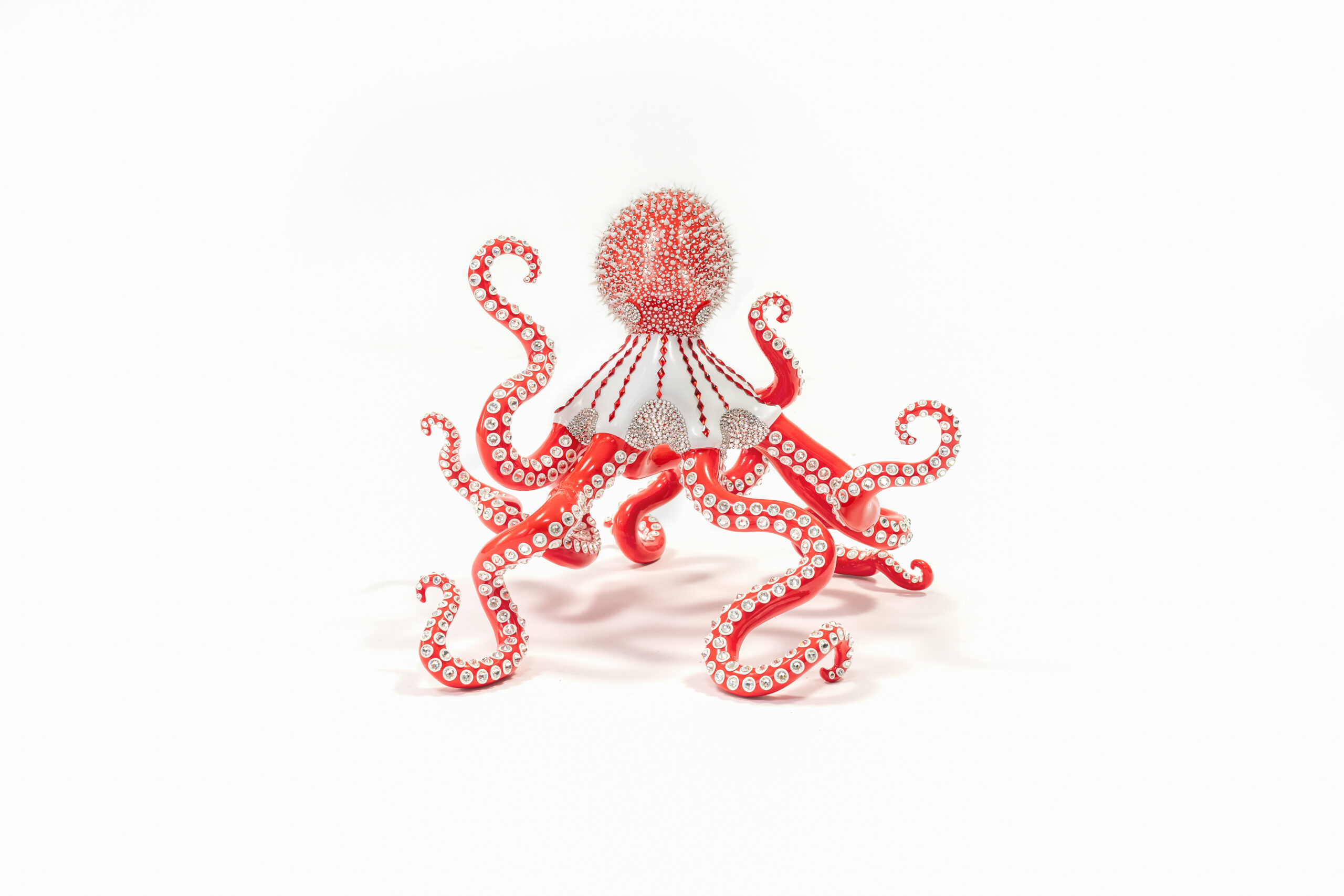 Poulpe Red and White – Eddy Maniez Poulpe Red and White van Eddy Maniez is een meesterlijk kunstwerk waarin kracht, luxe en speelsheid samenkomen. De sculptuur toont een imposante octopus, uitgevoerd in een opvallende combinatie van felrood en helder wit. De tentakels kronkelen sierlijk in verschillende richtingen, wat de sculptuur een dynamische en bijna dansende uitstraling geeft. Elk oppervlak is rijkelijk bezet met Swarovski kristallen en silicone dots, die het kunstwerk laten fonkelen bij iedere lichtinval. Bovendien benadrukt Poulpe Red and White de symboliek van de octopus: mysterie, intelligentie en aanpassingsvermogen. Door de combinatie van kleuren en materialen geeft Maniez dit zeedier een glamoureuze, moderne interpretatie. Het resultaat is een sculptuur die niet alleen de kracht van de natuur viert, maar ook een luxueus statement vormt. Het contrast tussen rood en wit versterkt de visuele impact, terwijl de kristallen een gevoel van elegantie en overdaad toevoegen. Dit werk overstijgt traditionele sculptuur. Het is een iconisch object dat iedere ruimte onmiddellijk transformeert. Poulpe Red and White nodigt uit tot bewondering en roept tegelijkertijd een gevoel van energie en verfijning op. Het is meer dan een kunstwerk; het is een blikvanger, een gespreksonderwerp en een symbool van extravagantie.