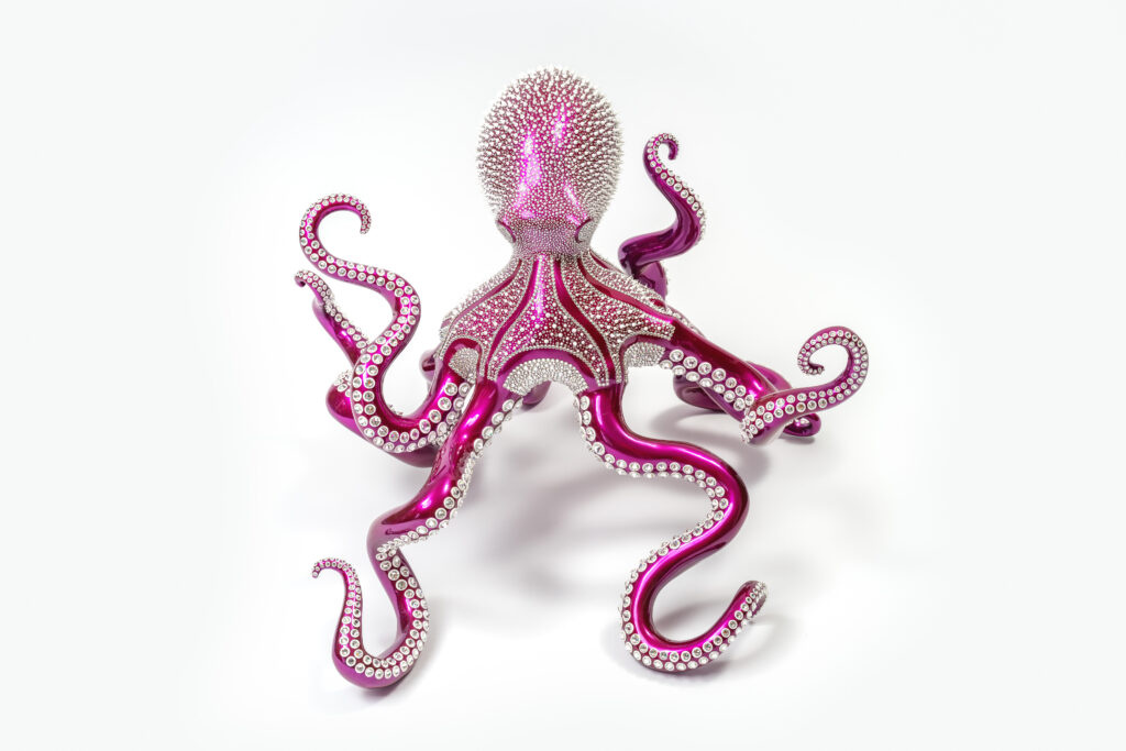 Poulpe Fuchsia – Eddy Maniez Poulpe Fuchsia van Eddy Maniez is een spectaculair kunstwerk waarin natuur en luxe samenkomen. De sculptuur toont een monumentale octopus, uitgevoerd in een diep glanzende fuchsia kleur en volledig bezet met talloze fonkelende kristallen. De sprankeling van het oppervlak geeft het werk een bijna magische uitstraling. Elk detail is zorgvuldig uitgewerkt: van de vloeiende lijnen van de tentakels tot de ritmische patronen van de kristallen. Het resultaat is een dynamisch beeld dat zowel elegantie als kracht uitstraalt. Bovendien weet Maniez met Poulpe Fuchsia een intrigerende symboliek over te brengen. De octopus staat bekend als een wezen vol mysterie, intelligentie en aanpassingsvermogen. In deze sculptuur krijgt het dier een glamoureuze en moderne interpretatie, waardoor het verandert in een symbool van luxe, overvloed en transformatie. De sierlijke beweging van de tentakels lijkt bijna dansend, alsof het kunstwerk tot leven komt zodra het licht de kristallen raakt. Het werk is meer dan een sculptuur; het is een statement piece dat iedere ruimte domineert. De combinatie van felle kleur, extravagante glans en verfijnde afwerking maakt het een eyecatcher die direct indruk maakt. Daarnaast nodigt het uit om dichterbij te komen en de oneindige details te bewonderen. Poulpe Fuchsia is een perfecte weerspiegeling van Maniez’ stijl: extravagant, kleurrijk en altijd vernieuwend. Het kunstwerk laat zien hoe hij traditionele sculpturale vormen weet te transformeren tot hedendaagse iconen die kunst en design samenbrengen.