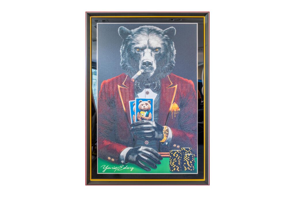 Yaniv Edery – Bear Pok’Art Red Suit is een kunstwerk dat direct kracht en elegantie uitstraalt. De imposante beer zit stijlvol aan de pokertafel, gekleed in een diep rood pak met zwarte accenten. Hij houdt zijn kaarten stevig vast, klaar om zijn tegenstanders te slim af te zijn. De gouden details, de horloge en de fiches versterken de uitstraling van luxe en macht. Dit werk vertelt een verhaal van strategie, spanning en dominantie. De beer symboliseert kracht, vastberadenheid en natuurlijke autoriteit. Zijn blik is intens en onvermurwbaar, alsof hij de controle volledig in handen heeft. De combinatie van poker en dierlijke kracht maakt dit kunstwerk zowel speels als indrukwekkend. Het rode pak is meer dan mode. Het staat voor lef, passie en energie. In combinatie met de donkere achtergrond en de lichte contrasten ontstaat er een compositie die blijft fascineren. Elk detail, van de rook van de sigaar tot de scherpe lijnen van het pak, is zorgvuldig uitgewerkt en ademt de typische stijl van Yaniv Edery. De symboliek van poker – risico, geduld en strategie – komt in dit werk perfect samen met de natuurkracht van de beer. Hierdoor ontstaat een kunstwerk dat uitnodigt tot reflectie, maar tegelijk een krachtige blikvanger is in elke ruimte.