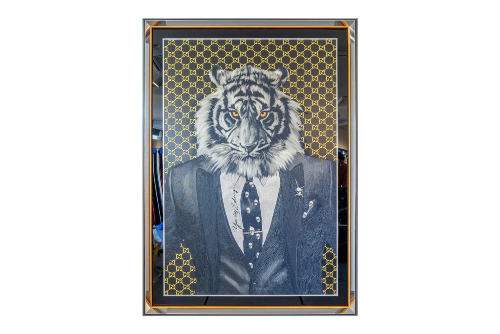 Yaniv Edery – Tiger Skull Yellow Suit Het kunstwerk Tiger Skull Yellow Suit van Yaniv Edery straalt kracht, stijl en mysterie uit. Het toont een trotse tijger, gekleed in een scherp gesneden pak, tegen een patroon van goud en geel. De combinatie van het wilde dier met elegante kleding creëert een spannend contrast. Het benadrukt zowel dierlijke kracht als menselijke verfijning. Dit contrast maakt het werk uniek en betekenisvol. Het kleurenpalet is zorgvuldig gekozen. De zwarte en grijze tinten van de tijger versterken de intensiteit van de goudgele achtergrond. Daardoor komt elke lijn en elke blik krachtig naar voren. De ogen van de tijger zijn fel en doordringend. Ze trekken de aandacht en geven het kunstwerk een aura van dominantie en elegantie. Dit detail maakt dat de toeschouwer blijft kijken. Yaniv Edery speelt met luxe en macht. Het strakke pak, de nette das en de subtiele details in reliëf versterken het gevoel van exclusiviteit. Het werk ademt status en symboliek. Met dit kunstwerk laat Edery zien hoe de grenzen tussen mode, kunst en natuur kunnen vervagen. Hij geeft de tijger een bijna menselijke uitstraling, terwijl de wilde kracht behouden blijft. Tiger Skull Yellow Suit is meer dan decoratie. Het is een statement. Een expressie van kracht, stijl en identiteit. Een werk dat uitnodigt tot reflectie en bewondering.