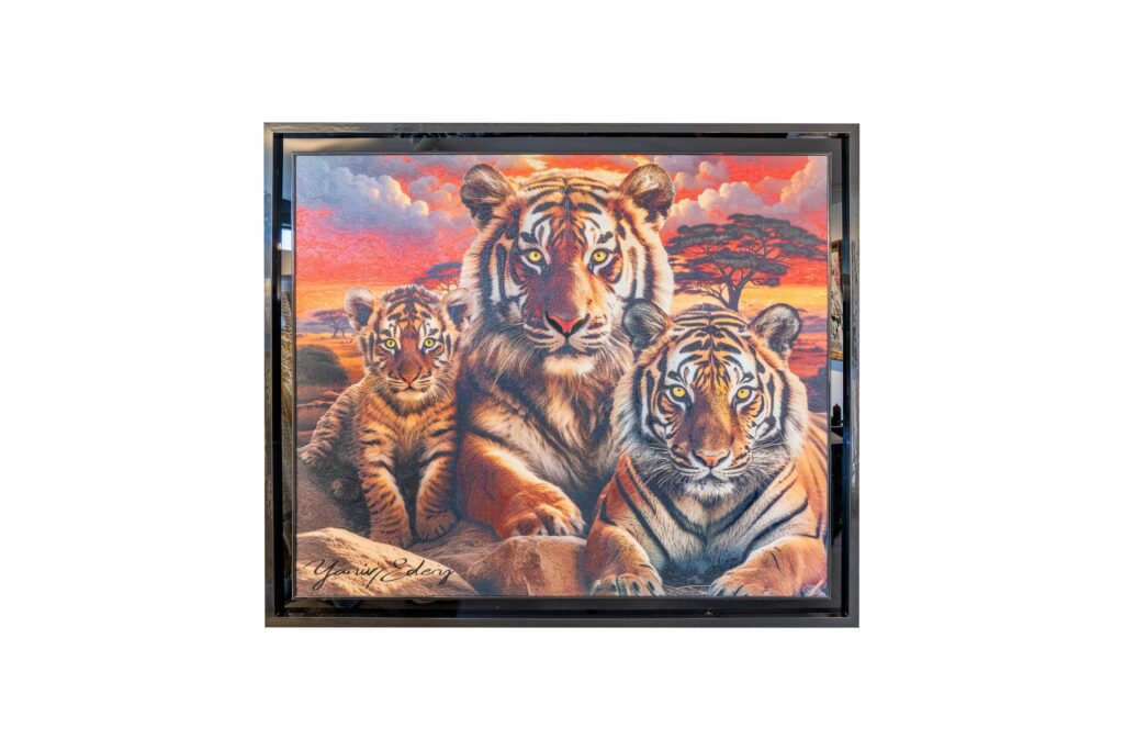 Yaniv Edery – Tiger Family Orange Dit indrukwekkende kunstwerk van Yaniv Edery toont een majestueuze tijgerfamilie in warme, oranje tinten. De volwassen tijgers en hun welp liggen dicht bij elkaar, wat kracht, bescherming en verbondenheid symboliseert. Hun indringende blikken grijpen direct de aandacht en maken het werk emotioneel sterk en visueel indrukwekkend. De achtergrond, met een vurige zonsondergang in oranje en rood, versterkt het gevoel van intensiteit en warmte. Het landschap ademt rust, maar ook mysterie. De tijgers, in volle glorie afgebeeld, vormen het hart van de compositie. Het contrast tussen hun krachtige gestalte en de serene omgeving maakt dit werk dynamisch en gelaagd. Edery weet met dit schilderij emoties op te roepen die verder gaan dan esthetiek. De volwassen tijgers staan voor kracht en wijsheid, terwijl het welpje symbool staat voor toekomst, groei en kwetsbaarheid. Deze combinatie creëert een universeel verhaal over familiebanden, bescherming en de continuïteit van het leven. De warme kleuren en de subtiele details in de vacht geven het werk levendigheid en diepte. De ogen van de tijgers lijken bijna tot leven te komen en trekken de kijker het schilderij in. Elk detail is zorgvuldig uitgewerkt en draagt bij aan de intensiteit van het geheel. Tiger Family Orange is meer dan een beeld van dieren; het is een ode aan de natuur en aan de kracht van verbondenheid. Het werk verrast telkens opnieuw en nodigt uit tot reflectie over kracht, liefde en balans.