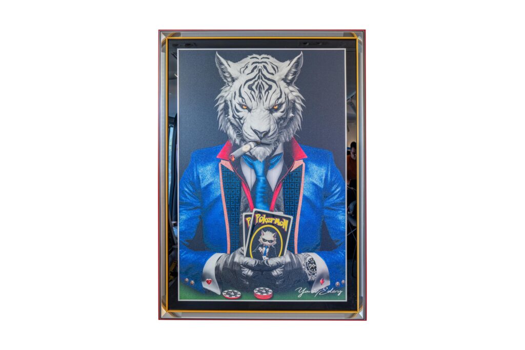 Yaniv Edery – Tiger Pok’Art Blue Suit Medium is een krachtig en intrigerend kunstwerk. Het toont een tijgerfiguur, stijlvol gekleed in een blauw pak, die met zelfverzekerde blik aan de pokertafel zit. De sigaar tussen de tanden en de kaarten in de hand versterken zijn dominante uitstraling. Dit werk ademt kracht, spanning en prestige. Het combineert speelse ironie met een luxueuze uitstraling, waardoor het onmiddellijk de aandacht trekt. De strakke lijnen, felle kleuren en scherpe contrasten maken dit kunstwerk een echte eyecatcher. De tijger symboliseert macht, moed en strategie, terwijl de pokerwereld staat voor risico, lef en succes. Samen creëren ze een verrassende visuele dialoog die blijft intrigeren. Dit werk is niet alleen een schilderij, het is een statement. Ideaal voor wie zijn interieur een iconische en eigentijdse uitstraling wil geven.