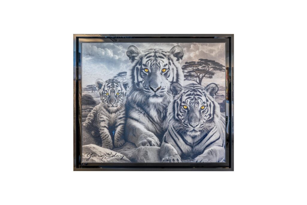 Yaniv Edery – Tigers Black And White Dit meesterwerk van Yaniv Edery toont de indrukwekkende kracht en zachtheid van een tijgerfamilie. In het midden staat de trotse moeder, omringd door haar welp en een volwassen tijger. Hun gele ogen lichten op in het monochrome palet en trekken direct de aandacht. Deze blik vol intensiteit en bescherming maakt het werk uniek en onvergetelijk. De keuze voor zwart-wit benadrukt kracht, eenvoud en puurheid. De tijgers lijken haast uit steen gehouwen, maar hun ogen brengen leven en emotie. Dit contrast geeft het kunstwerk een mystieke uitstraling. Het beeld vertelt een verhaal van verbondenheid, zorg en oerkracht. Het roept respect en bewondering op, maar ook een gevoel van rust en stabiliteit. De achtergrond met de Afrikaanse boom en rotsachtige vlakte versterkt het gevoel van natuur en vrijheid. Elk detail is met precisie uitgewerkt: de strepen van de vachten, de gespierde lichamen, de zachte expressie van het welpje. Dit maakt het werk niet enkel decoratief, maar ook een symbool van familie en bescherming. Plaats dit kunstwerk in een woonkamer, kantoor of galerie en ervaar hoe het direct een krachtige sfeer schept. Het is niet zomaar een kunstwerk, maar een statement. Het straalt energie, balans en elegantie uit. Perfect voor wie houdt van natuur, dieren en symboliek.