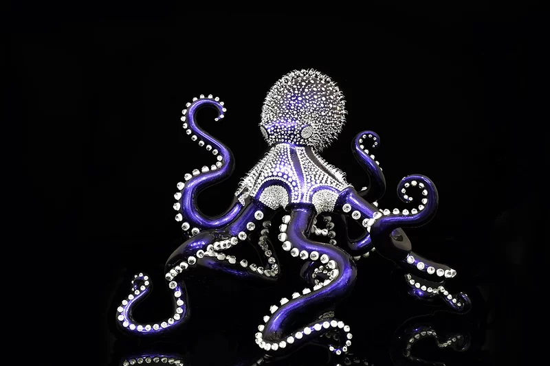 Poulpe Blue (klein) – Eddy Maniez Poulpe Blue van Eddy Maniez is een meesterlijk kunstwerk waarin elegantie, kracht en extravagantie samensmelten. De sculptuur toont een majestueuze octopus, uitgevoerd in een diepe, glanzende blauwtint en rijkelijk bezet met sprankelende kristallen. De weelde van details zorgt ervoor dat elk tentakel schittert zodra het licht het oppervlak raakt. Het beeld straalt een hypnotiserende energie uit en weet de toeschouwer direct te betoveren. Bovendien benadrukt Poulpe Blue de mysterieuze en intelligente aard van de octopus, een dier dat symbool staat voor transformatie, aanpassingsvermogen en kracht. In handen van Maniez krijgt dit zeedier een bijna mythische allure. De fonkelende kristallen veranderen de sculptuur in een luxueus statement piece dat zowel modern als tijdloos aanvoelt. Het contrast tussen de donkere achtergrond en de felle schittering van het object versterkt de dramatische impact. Het werk is meer dan een sculptuur; het is een icoon van extravagantie en verfijning. Elke curve, elke lijn en elk kristal is zorgvuldig geplaatst, wat de toewijding en precisie van Maniez onderstreept. Poulpe Blue is daarmee niet alleen een eerbetoon aan de oceaan, maar ook een expressie van pure kunstzinnige luxe.