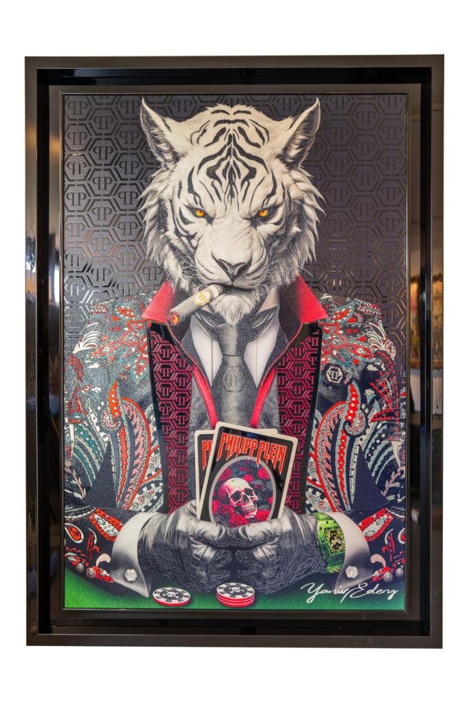 Yaniv Edery – Tiger Poker Philipp Plein Black and Red is een kunstwerk dat luxe en kracht samenbrengt. De witte tijger, symbool van dominantie en strategie, staat centraal. Hij rookt een sigaar, houdt kaarten stevig vast en straalt absolute zelfverzekerdheid uit. De intensiteit van zijn blik maakt meteen indruk. De combinatie van zwart en rood in het Philipp Plein-pak versterkt de spanning. Het patroon is rijk, gedetailleerd en extravagant. Hierdoor krijgt de tijger niet alleen autoriteit, maar ook stijl en moderniteit. Het is een werk dat energie en luxe uitstraalt. Het poker-element voegt een extra laag toe. Poker is een spel van strategie, durf en geduld. Precies dat weet Edery te vertalen naar dit beeld. De fiches, kaarten en details benadrukken dat hier meer speelt dan een spel. Het is een strijd om macht en controle. Elk detail is zorgvuldig geplaatst. Daardoor voelt het werk levendig en krachtig. De contrasterende kleuren zorgen voor spanning, terwijl de compositie balans en harmonie behoudt. Dit kunstwerk is daarmee meer dan decoratie. Het is een statement, een blikvanger die een ruimte volledig transformeert. Wie dit werk ziet, voelt de intensiteit. Het nodigt uit om stil te staan, te observeren en de kracht van de tijger te ervaren. Dit is kunst die blijft fascineren.