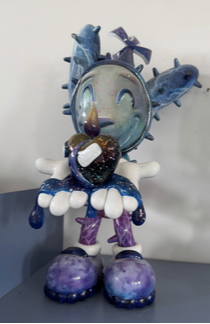 Kakkie Sculpture – Loes van Delft Met Kakkie Sculpture brengt Loes van Delft haar iconische stijl tot leven in driedimensionale vorm. Dit speelse en tegelijk ontroerende beeld straalt energie, humor en emotie uit. Het karakter Kakkie, herkenbaar met grote schoenen, expressieve handen en een stralend gezicht, houdt een glanzend hart vast dat overloopt van kleur en symboliek. Daardoor wordt dit werk niet alleen een sculptuur, maar ook een krachtige vertelling over liefde en kwetsbaarheid. Allereerst valt de levendige kleurencombinatie op: blauw, paars en metallic accenten versterken de dynamiek van het beeld. Vervolgens zie je de zorgvuldig uitgewerkte details die de typische cartooneske stijl van Van Delft herkenbaar maken. Bovendien geeft de speelse houding van Kakkie een gevoel van vreugde en optimisme. Juist dit maakt de sculptuur aantrekkelijk voor een breed publiek. Deze sculptuur is meer dan decoratief: het is een exclusief kunstwerk met duidelijke verzamelwaarde. Door haar internationale reputatie zijn de beelden van Loes van Delft bijzonder gewild bij zowel beginnende als ervaren verzamelaars.